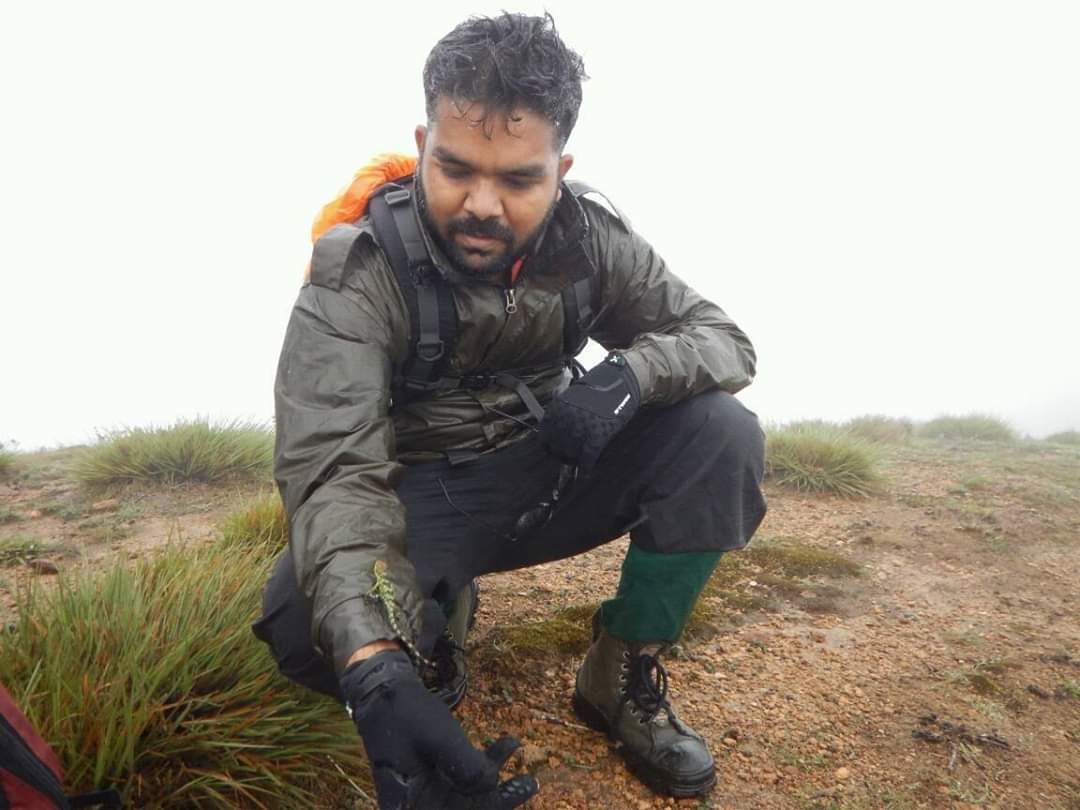 Nikunj Jambu crouched on a grassland ridge during a field survey